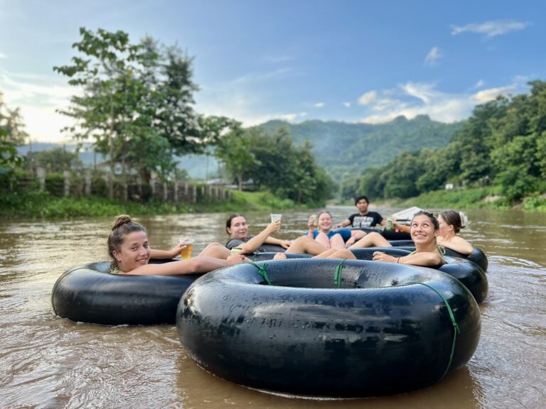 Guests floating the Mae Taeng in tied-together tubes with drinks in hand as the light turns golden