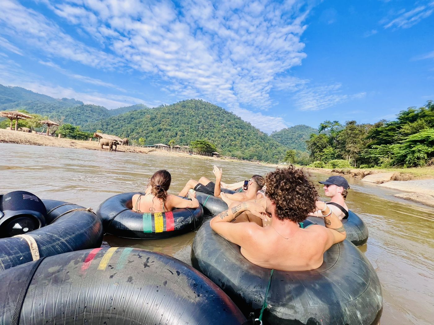 A group of travellers drifting side by side in tubes down the Mae Taeng river, jungle mountains all around