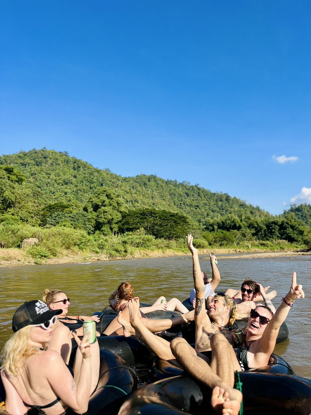 Travellers cheering with arms in the air while floating in tubes on the river